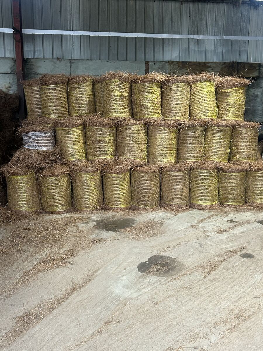 Round bales stacked three high under a barn roof, tied with yellow twine