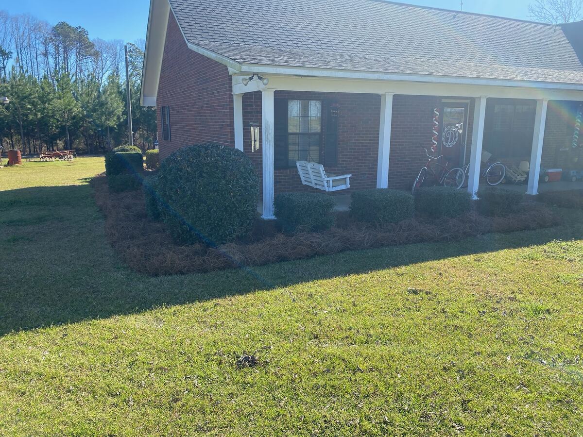 A porch with the beds in front of it freshly spread with pine straw